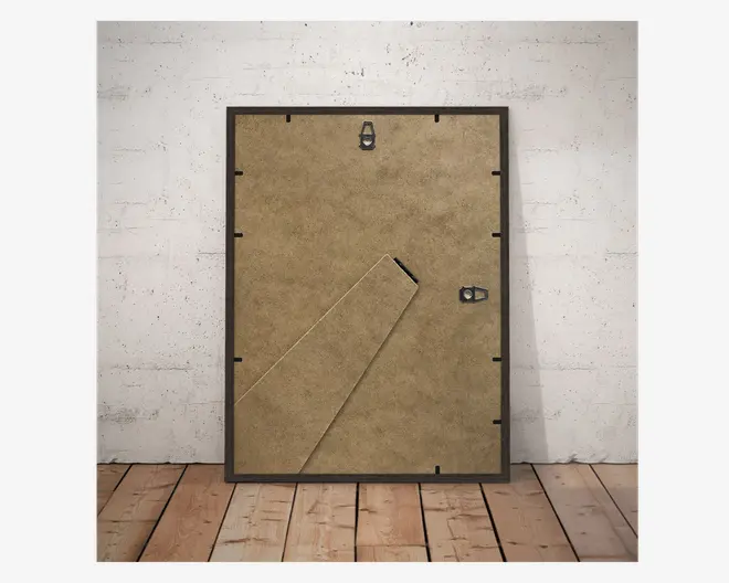 Billedet viser bagsiden af en rektangulær ramme med brun MDF-bagside. Rammen har en udfoldelig støttefod til placering på bord, en metalophængskrog øverst til vægmontering samt en ekstra metalflap i højre side for sikker lukning. Kanterne på bagsiden holdes fast af flere sorte drejetapper.