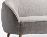 Nærbillede af en stol med lysegråt tekstureret stofbetræk, afrundet armlæn og ryglæn samt lyse træben. Stoffet ser blødt og slidstærkt ud, og stolens form er moderne og indbydende.