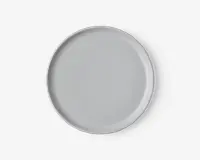 Rund tallerken med en glat, mat lysegrå overflade og en let forhøjet kant. Designet er minimalistisk og moderne uden mønstre eller dekorationer.