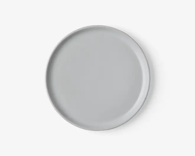 Rund tallerken med en glat, mat lysegrå overflade og en let forhøjet kant. Designet er minimalistisk og moderne uden mønstre eller dekorationer.