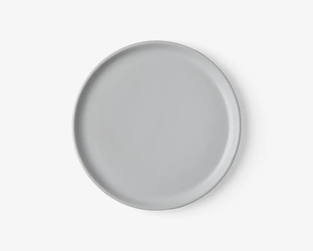 Rund tallerken med en glat, mat lysegrå overflade og en let forhøjet kant. Designet er minimalistisk og moderne uden mønstre eller dekorationer.