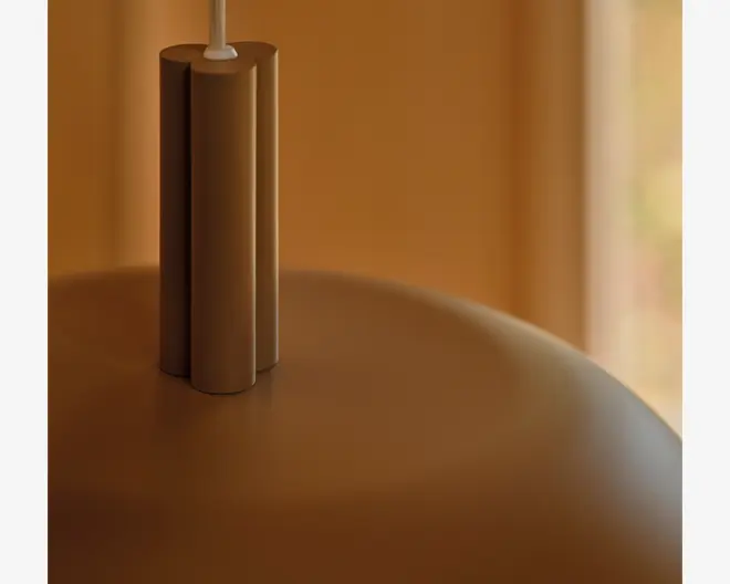 Nærbillede af en varm brun, rund lampe med en lodret cylindrisk topdel og en hvid ledning, der går ud fra toppen.