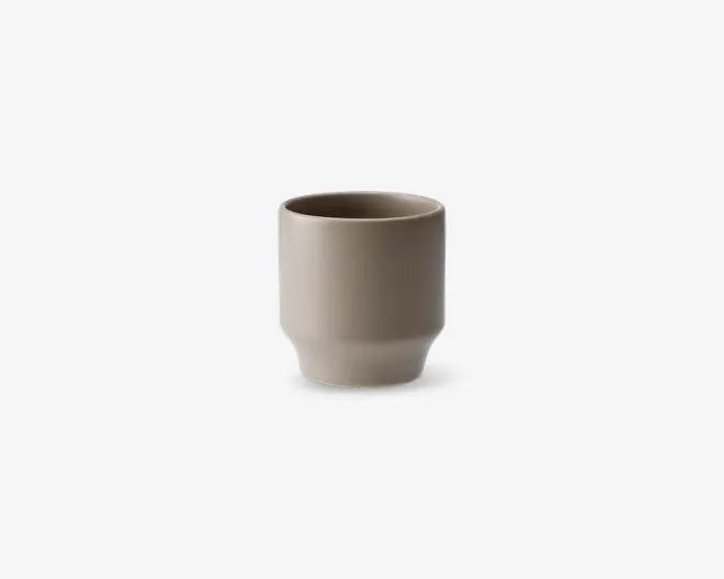 En minimalistisk, cylindrisk kop med en glat mat beige overflade. Koppen har lige sider og en let afrundet bund, uden hank eller dekorative detaljer. Det enkle design giver et moderne og elegant udtryk.