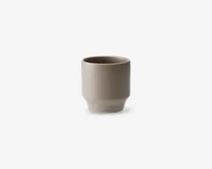 En minimalistisk, cylindrisk kop med en glat mat beige overflade. Koppen har lige sider og en let afrundet bund, uden hank eller dekorative detaljer. Det enkle design giver et moderne og elegant udtryk.
