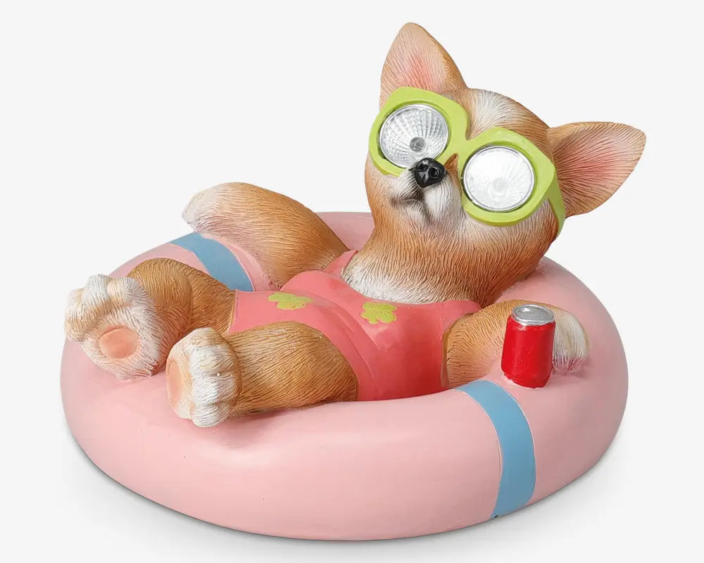 En dekorativ figur af en afslappet hund iført lyserød badedragt og grønne solbriller, der ligger på en lyserød og blå oppustelig badering. Hunden har realistisk pelsstruktur, store spidse ører og holder en rød sodavandsdåse. Solbrillerne har reflekterende linser, hvilket giver et sjovt udtryk.