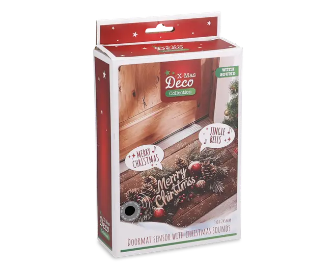 Rektangulær emballage med et festligt design i rød og hvid, dekoreret med stjerner og julemotiver. Forsiden viser et billede af en dørmåtte pyntet med kogler, røde bær og teksten 'Merry Christmas'. Kassen fremhæver, at produktet har en sensor, der afspiller julesange som 'Merry Christmas' og 'Jingle Bells', når den aktiveres. Emballagen angiver også måttens mål (ca. 30 x 71 cm) og at den er en del af X-Mas Deco Collection.
