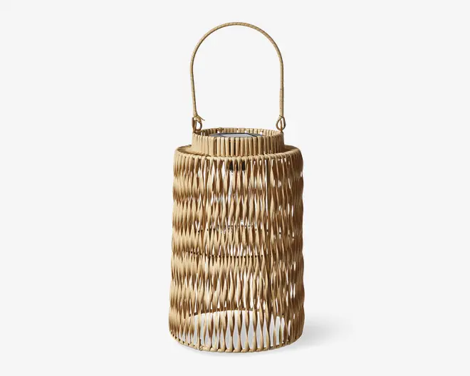 Høj, cylindrisk kurv med naturligt flettet rattan-design, der har et lodret zigzag-mønster og et buet håndtag fastgjort øverst. Den åbne fletning gør det muligt at se igennem siderne, og håndtaget er solidt for nem transport. Kurven har en glat, poleret overflade og en neutral, lysebrun farve.