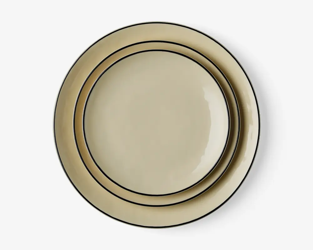 Sæt med to runde tallerkener i en lys beige farve med blank overflade. Hver tallerken har et enkelt, elegant design med en tynd mørk kant langs randen og en ekstra mørk linje tættere på midten, hvilket giver et klassisk og diskret udtryk. Tallerkenerne er stablet, så størrelsesforskellen er synlig.