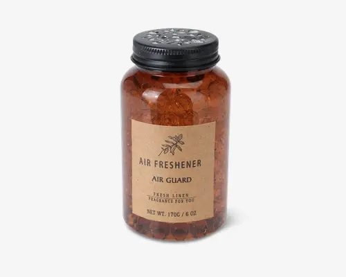 Plastikbeholder i ravfarve med sort, ventileret skruelåg. Beholderen indeholder gennemsigtige gelékugler og har en brun papiretikette med enkel sort tekst og en lille botanisk illustration. Etiketten lyder: "Air Freshener, Air Guard, Fresh Linen Fragrance For You." Designet er minimalistisk og naturligt, hvilket antyder en frisk og ren duft.
