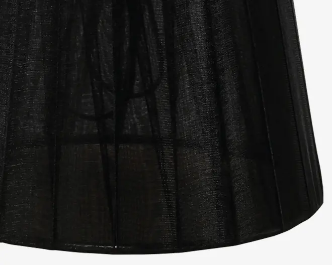 Nærbillede af sort, gennemsigtigt stof med diskret lodret stribemønster. Materialet er let og halvgennemsigtigt, så noget lys kan trænge igennem. Kanterne er pænt afsluttede, og stoffet falder glat, hvilket antyder en blød og let struktur.
