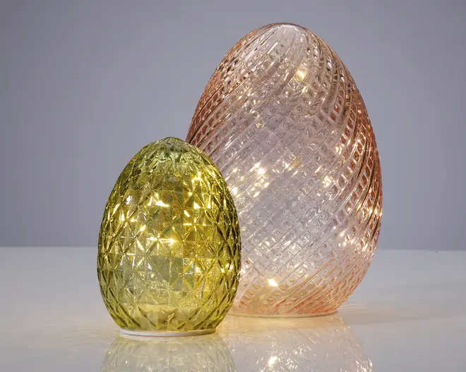 To dekorative, æggeformede glasornamenter med en tekstureret, diamantmønstret overflade. Den mindre ornament er grøn, mens den større er lyserød. Begge ornamenter er oplyst indefra af små LED-lys, hvilket skaber en varm, glødende effekt. Glasset har en blank finish, og lyset fremhæver det indviklede mønster på hver del.