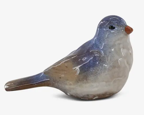 Keramisk fuglefigur med blank overflade, der har en blanding af blå, brune og cremefarvede nuancer. Fuglen har en glat, rund krop, et lille orange næb og sorte øjne. Overfladen viser diskrete farveovergange og nuanceringer, hvilket giver et naturtro udseende. Figuren er kompakt og detaljeret, velegnet som dekoration.