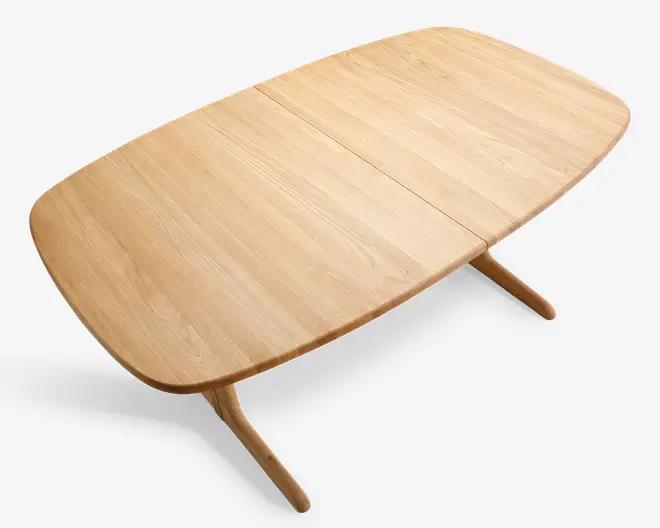 Rektangulært bord i lyst egetræ med blødt afrundede hjørner og en glat overflade. Bordpladen har en diskret samling i midten, hvilket tyder på, at det kan udvides. Benene er let skrå og afrundede, hvilket giver et moderne og minimalistisk udtryk.