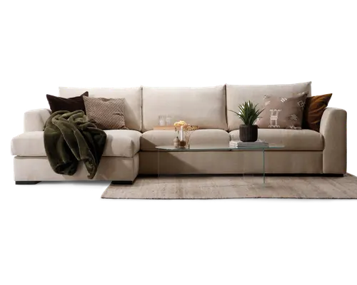 Rummelig L-formet sofa betrukket med lysebeige stof, udstyret med brede, bløde sæde- og ryghynder for ekstra komfort. Sofaen er pyntet med forskellige pyntepuder i brune, beige og mønstrede designs samt et mørkegrønt tæppe lagt over den ene armlæn. Foran sofaen står et minimalistisk sofabord i glas med en potteplante, bøger og dekorative genstande. Opsætningen står på et neutralt farvet tæppe, hvilket skaber en hyggelig og indbydende stue.