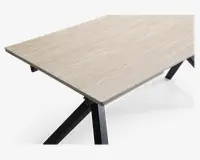 Rektangulær bordplade med en lys beige, marmorlignende overflade og diskrete årer. Overfladen ser glat og let blank ud. Bordet understøttes af solide, skråtstillede sorte metalben, hvilket giver det et moderne og minimalistisk udtryk.