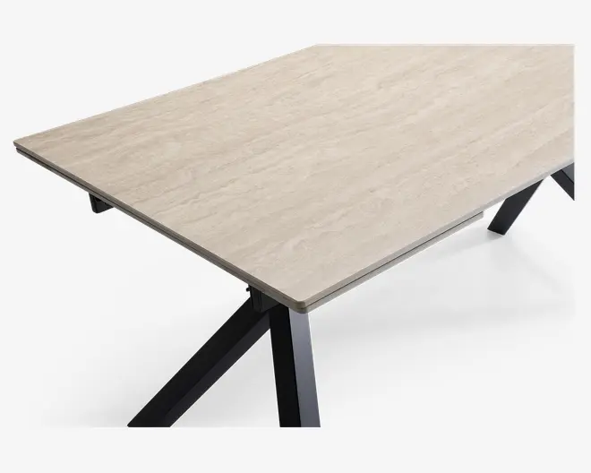 Rektangulær bordplade med en lys beige, marmorlignende overflade og diskrete årer. Overfladen ser glat og let blank ud. Bordet understøttes af solide, skråtstillede sorte metalben, hvilket giver det et moderne og minimalistisk udtryk.