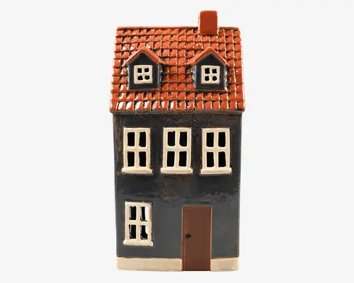 Dekorativt hus i keramik med blank mørkeblå facade, hvide vinduesrammer og brun dør. Taget har en tekstur af orange-røde tegl og to små kvistevinduer. En skorsten sidder på højre side af taget. Designet er detaljeret og charmerende, velegnet til udstilling eller som samlerobjekt.