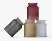 Sæt med fire cylindriske beholdere lavet af mat glas, hver med lodret rillet tekstur. Beholderne fås i fire farver: dæmpet rød, olivengrøn, beige og gennemsigtig hvid. Hver har en bred åbning og en kort hals, velegnet til at holde blomster eller dekorative genstande.