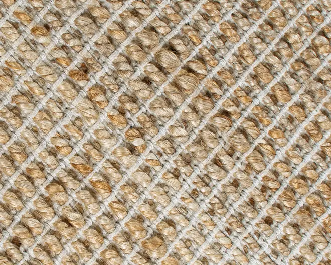 Nærbillede af en tekstureret vævet overflade med tykke, naturlige jutefibre i en lys beige farve. Væveteknikken danner et diskret diagonalt gittermønster med hævede, kraftige løkker, hvilket giver materialet et rustikt og slidstærkt udtryk. Fibrene har lette farvevariationer, som tilføjer dybde og et naturligt udseende.