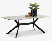 Rektangulært bord med en lys træbordplade og sorte metalben, der er vinklet udad for stabilitet. Bordpladen er dekoreret med en sort rillet urtepotte med en grøn plante, et blåt snoet stearinlys i en guldfarvet stage, en stak bøger, et par briller og en appelsin. Bordet har et moderne, minimalistisk design med rene linjer og en solid ramme.