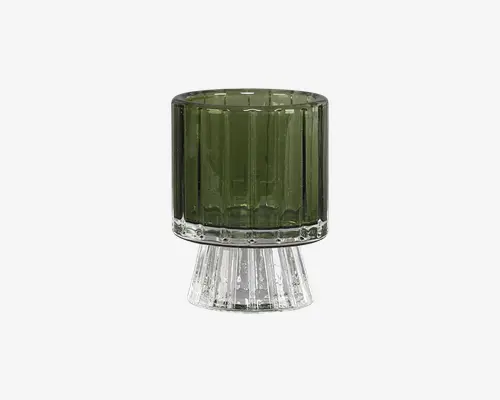 Et lille, cylindrisk glas med en mørkegrøn, lodret rillet overdel og en klar, udvidet fod. Glasset har et moderne, geometrisk design med rene linjer og et robust udtryk.