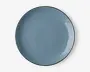 En rund, flad tallerken med en glat, blank overflade i en afdæmpet blå farve. Tallerkenen har en let hævet kant og et minimalistisk, moderne design. Overfladen er jævn og reflekterende med diskrete variationer i glasuren, som giver karakter.