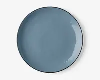 En rund, flad tallerken med en glat, blank overflade i en afdæmpet blå farve. Tallerkenen har en let hævet kant og et minimalistisk, moderne design. Overfladen er jævn og reflekterende med diskrete variationer i glasuren, som giver karakter.
