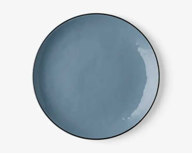 En rund, flad tallerken med en glat, blank overflade i en afdæmpet blå farve. Tallerkenen har en let hævet kant og et minimalistisk, moderne design. Overfladen er jævn og reflekterende med diskrete variationer i glasuren, som giver karakter.