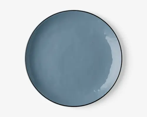 En rund, flad tallerken med en glat, blank overflade i en afdæmpet blå farve. Tallerkenen har en let hævet kant og et minimalistisk, moderne design. Overfladen er jævn og reflekterende med diskrete variationer i glasuren, som giver karakter.