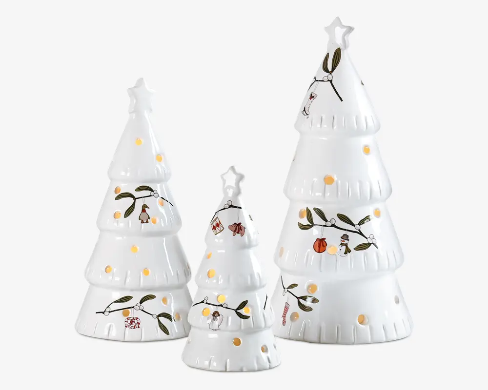 Sæt med tre hvide keramiske juletræsdekorationer i forskellige størrelser, hver med en stjerne på toppen. Overfladerne er dekoreret med malede, festlige motiver som fugle, snemænd, julekugler og kristtjørn. Små runde udskæringer er spredt over træerne, så lys kan skinne igennem og skabe en glødende effekt, når de er oplyst indefra.