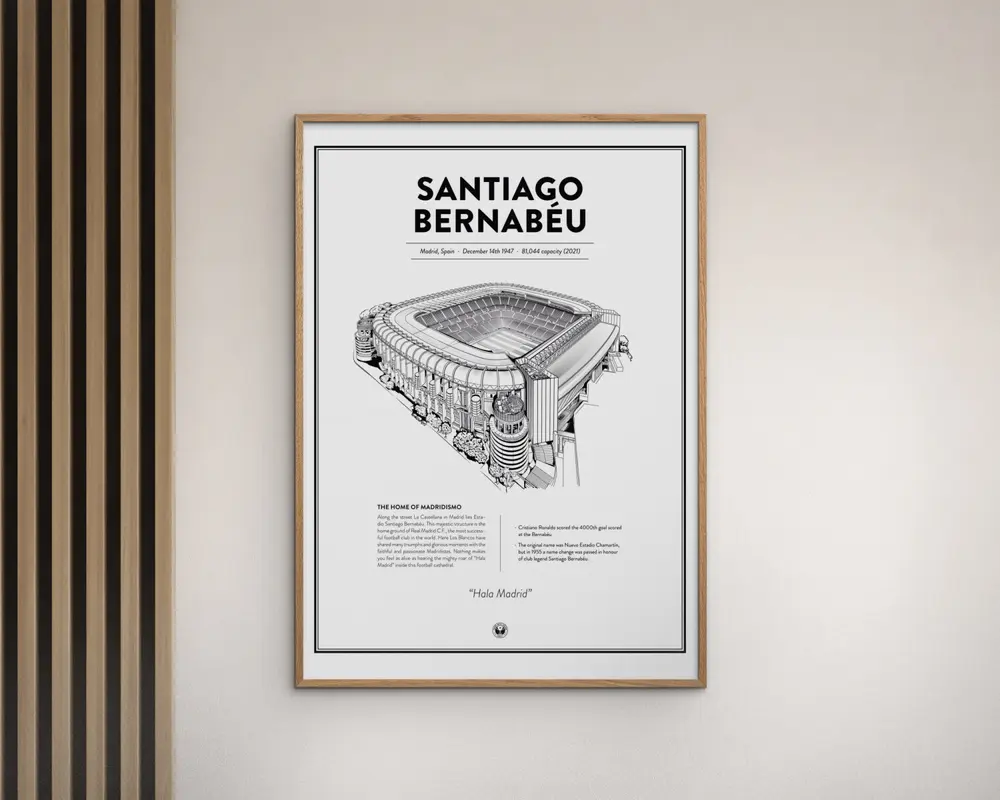 En indrammet plakat med en detaljeret sort-hvid arkitektonisk illustration af Santiago Bernabéu-stadionet. Plakaten har stadionets navn med store bogstaver øverst, efterfulgt af oplysninger som placering, åbningsdato og kapacitet. Under illustrationen er der en tekstblok med beskrivelse og statistik om stadionet. Rammen er enkel og lavet af lyst træ, og plakaten har et minimalistisk design med hvid baggrund og en tynd sort kant.