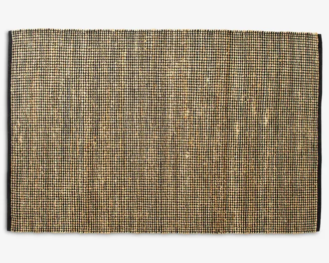 Rektangulært vævet underlag med tæt struktur og naturlige farver i brune og beige nuancer. Overfladen har et diskret ternet mønster, som opstår ved sammenfletningen af fibrene, hvilket giver et rustikt og organisk udtryk. Kanterne er lige og pænt afsluttede, hvilket sikrer holdbarhed og et rent udseende.