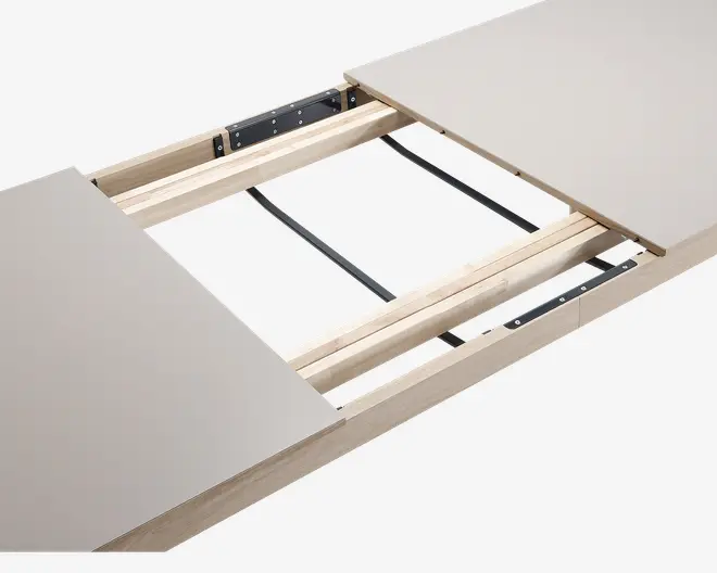 Nærbillede af et bord med udtræksmekanisme, hvor to bordplader er adskilt for at vise de indvendige træskinner og metalbeslag. Designet gør det muligt at tilføje en ekstra plade for at forlænge bordet. Bordpladen har en glat, lys overflade, og rammen er lavet af lyst træ.