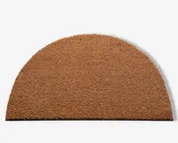En halvcirkelformet måtte lavet af grove, naturlige brune fibre. Overfladen har en ru tekstur, der egner sig til at skrabe snavs af sko. Kanterne er pænt skåret, og måtten har en ensartet farve og tykkelse over hele fladen.