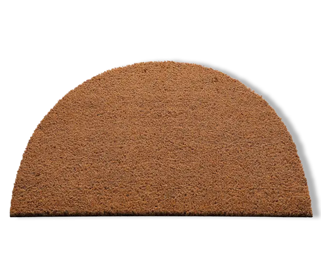 En halvcirkelformet måtte lavet af grove, naturlige brune fibre. Overfladen har en ru tekstur, der egner sig til at skrabe snavs af sko. Kanterne er pænt skåret, og måtten har en ensartet farve og tykkelse over hele fladen.