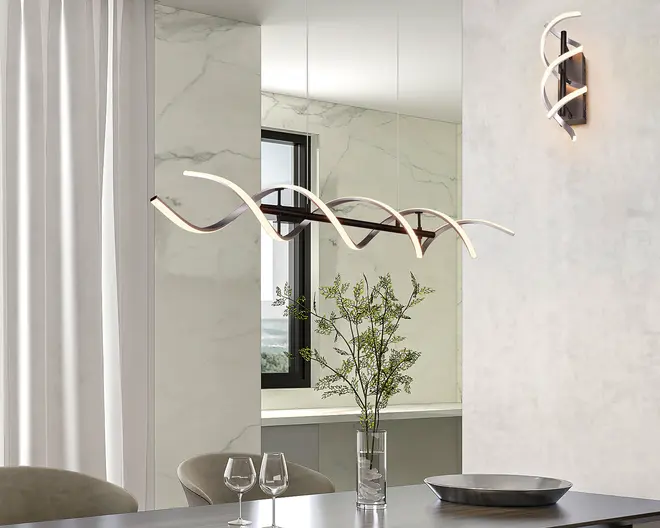 Et moderne lysarmatur med et skulpturelt, bølgeformet design, hvor sammenflettede LED-strips danner en elegant form. Armaturet hænger fra loftet i tynde wirer, hvilket giver et svævende udtryk. LED-stripsene udsender et blødt, varmt hvidt lys, og selve armaturet har en slank, mørk metalfinish. Designet er minimalistisk og nutidigt, velegnet til spise- eller opholdsrum.