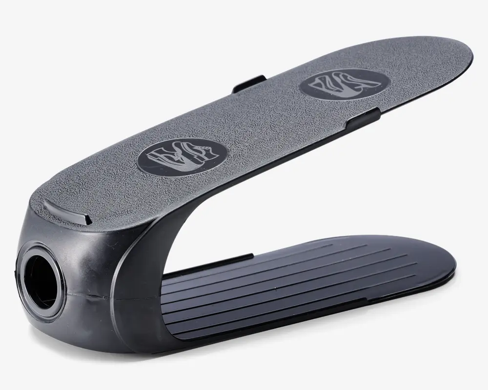 Sort skoopbevarer i plast med to niveauer, der har en tekstureret, skridsikker overflade øverst med to cirkulære gribemønstre og en rillet bundplatform. Organisatoren har en buet, åben struktur, så én sko kan placeres ovenpå og én nedenunder, hvilket optimerer den lodrette opbevaringsplads.