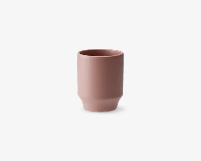 En minimalistisk, cylindrisk kop med en mat støvet rosa finish. Koppen har lige sider med en let indsnævring nær bunden, hvilket giver et moderne og elegant udtryk. Randen er glat og let afrundet for behagelig drikning. Overfladen er glat og uden dekoration, hvilket understreger det enkle, moderne design.