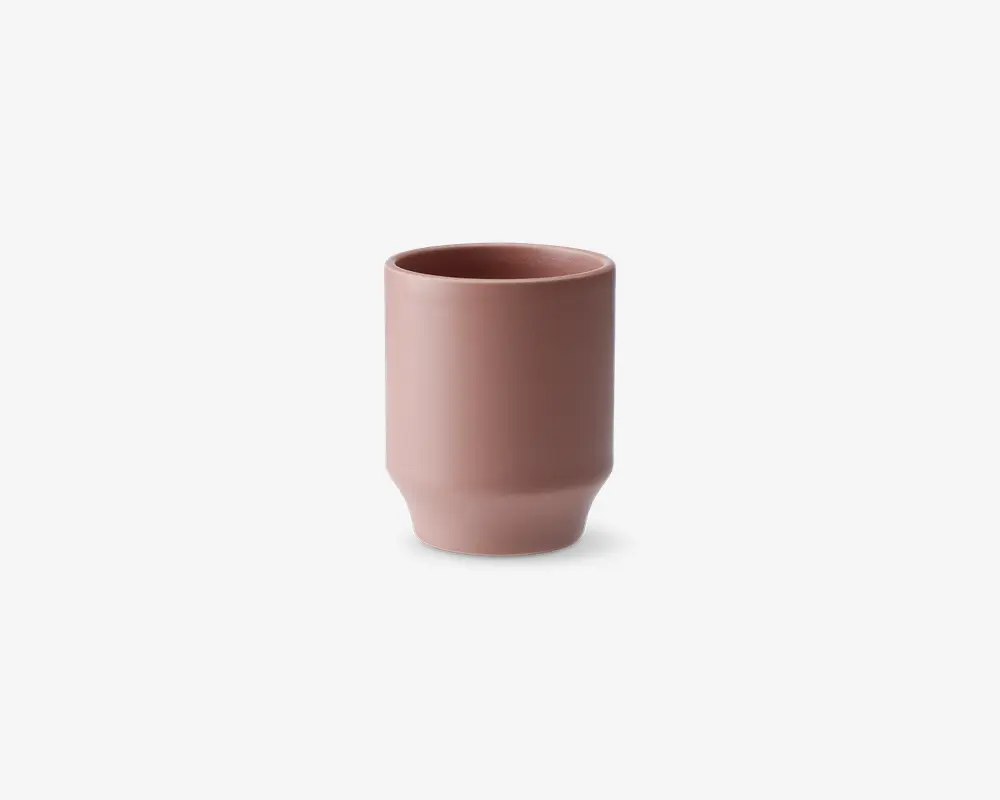 En minimalistisk, cylindrisk kop med en mat støvet rosa finish. Koppen har lige sider med en let indsnævring nær bunden, hvilket giver et moderne og elegant udtryk. Randen er glat og let afrundet for behagelig drikning. Overfladen er glat og uden dekoration, hvilket understreger det enkle, moderne design.
