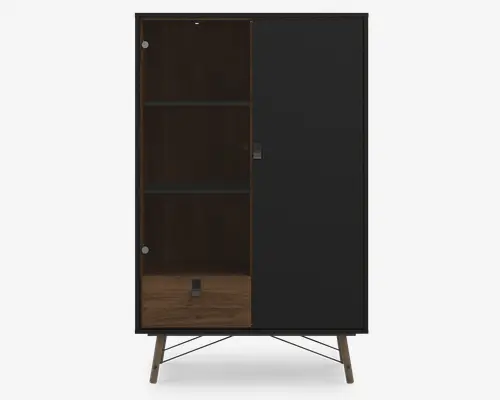 Moderne skab med mat sort finish, der har to låger: én i solid sort og én i gennemsigtig glas. Indvendigt er der to hylder til opbevaring eller udstilling, og skabet står på skrå, træben for et retro-inspireret udtryk. Glaslågen har to synlige, runde hængsler, og designet er enkelt og stilrent.