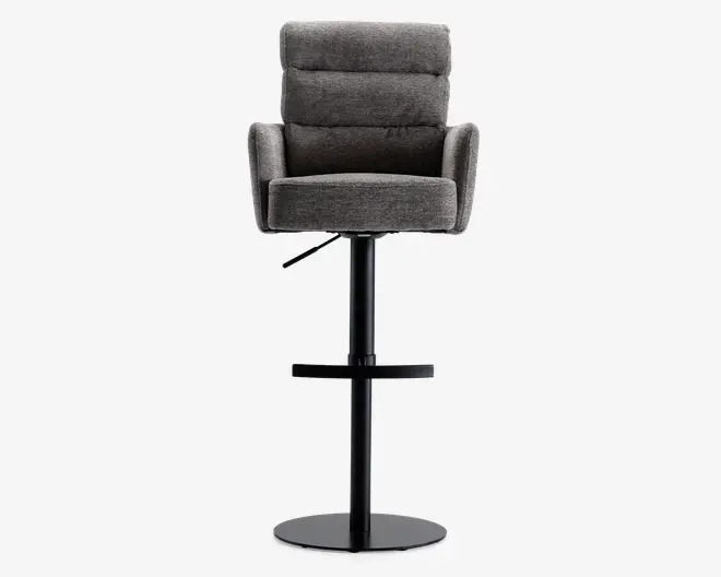 En moderne barstol med et blødt, mørkegråt polstret sæde og ryglæn med vandrette syninger. Stolen har polstrede armlæn og et bredt, komfortabelt sæde. Den står på en sort metalfod med en rund fodstøtte og en flad, rund base for stabilitet. Højden kan justeres med et håndtag under sædet.
