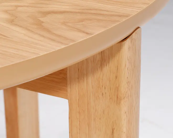 Nærbillede af et hjørne på et træbord, hvor den glatte, afrundede kant på bordpladen og de solide, rektangulære ben ses tydeligt. Træets årer er synlige, og finishen fremstår naturlig og lys, hvilket fremhæver håndværket og den sømløse samling mellem bordplade og ben.