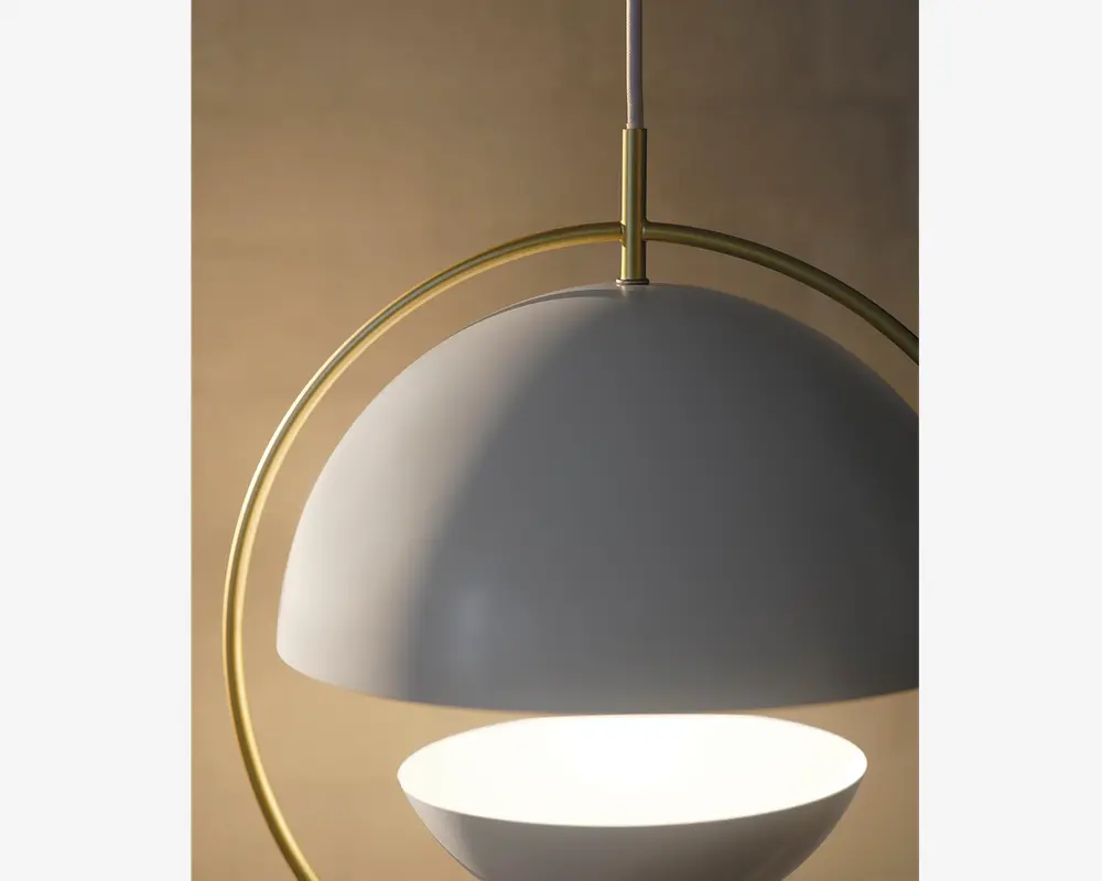 Nærbillede af en moderne pendellampe med en mat hvid, halvkugleformet skærm og en tilsvarende hvid, skålformet diffuser nedenunder. Lampen har en elegant bueformet ramme i messing eller guldmetal, som giver et stilfuldt udtryk. Lampen hænger fra en lodret stang, og designet er minimalistisk og nutidigt.