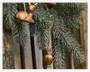 Nærbillede af frostbelagte grangrene med to metalliske guldfarvede dyreornamenter hængende. Det ene ornament forestiller en ugle med detaljerede fjer og ansigtstræk, mens det andet, som er lidt ude af fokus, ligner et rådyr. Ornamenterne har en mat overflade og hænger i tynde snore, hvilket giver et festligt og elegant udtryk til de naturlige grene.