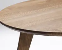 Nærbillede af en rund bordplade i træ med en glat, naturlig finish. Træets årer er tydelige og giver et varmt og organisk udtryk. Bordpladens kant er let affaset, og et solidt, skråt ben ses delvist, i samme træfarve som bordpladen.