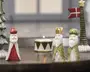 Små dekorative figurer af de tre vise mænd med hvide skæg og kåber i guld, rød og grøn, vist sammen med en stribet fyrfadsstage og et højt træ med en stjerne og et rødt flag.