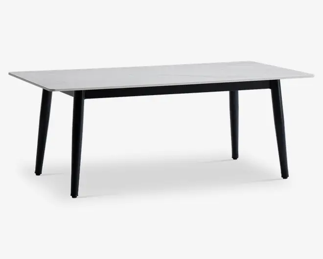 Rektangulært bord med en glat, hvid bordplade og fire let skråtstillede sorte ben. Designet er minimalistisk og moderne med rene linjer og en slank profil. Bordet virker solidt og rummeligt, velegnet til spisning eller arbejde.