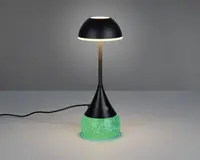 Moderne bordlampe med sort, kuppelformet skærm og en slank, central stang. Basen er konisk med en berøringsfølsom tænd/sluk-knap og har en glødende grøn, tekstureret overflade, der giver en dekorativ effekt. Lampen er tilsluttet med en synlig ledning.