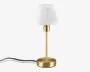Denne lampe har et slankt, moderne design med en cylindrisk fod og stang i guldfarvet metal. Lampeskærmen er lavet af hvidt, marmoreret glas, hvilket giver et blødt og diffust lys, når lampen er tændt. Lampen har et kompakt design, der gør den velegnet til natborde eller skriveborde. Strømledningen er synlig og går ud fra lampens fod.