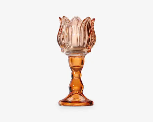 Dekorativ lysestage i glas med en gennemsigtig ravfarvet tone. Toppen har et kronbladslignende design, der minder om en udsprunget blomst, mens stagen har en elegant formet stilk med afrundede konturer og en bred, stabil fod. Glasset har en blank overflade, som fremhæver det dekorative udtryk.
